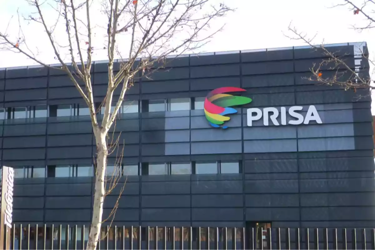 Fachada de un edificio moderno con el logo de PRISA y un árbol sin hojas en primer plano Fachada de un edificio moderno con el logo de PRISA y un árbol sin hojas en primer plano