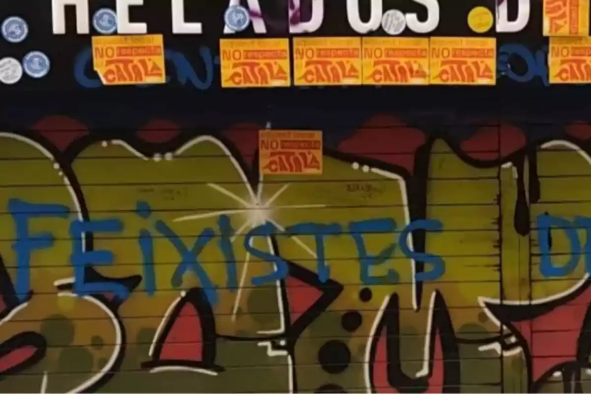 Persiana de local con grafiti colorido y la palabra feixistes pintada en azul junto a varias pegatinas naranjas y blancas Persiana de local con grafiti colorido y la palabra feixistes pintada en azul junto a varias pegatinas naranjas y blancas