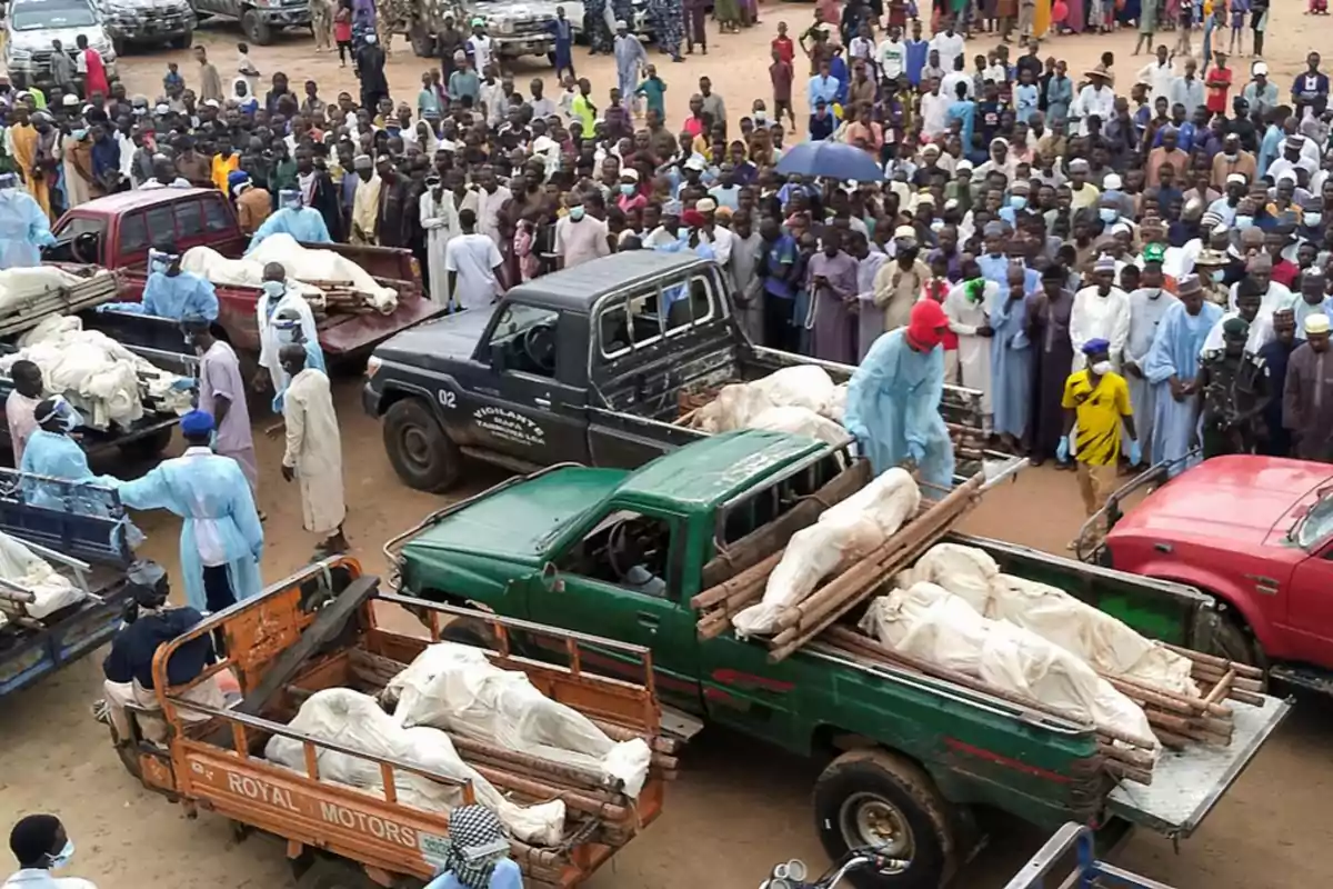 Varias camionetas transportan cuerpos envueltos en mantas blancas mientras una multitud de personas observa en un ambiente de tensión y tristeza Varias camionetas transportan cuerpos envueltos en mantas blancas mientras una multitud de personas observa en un ambiente de tensión y tristeza