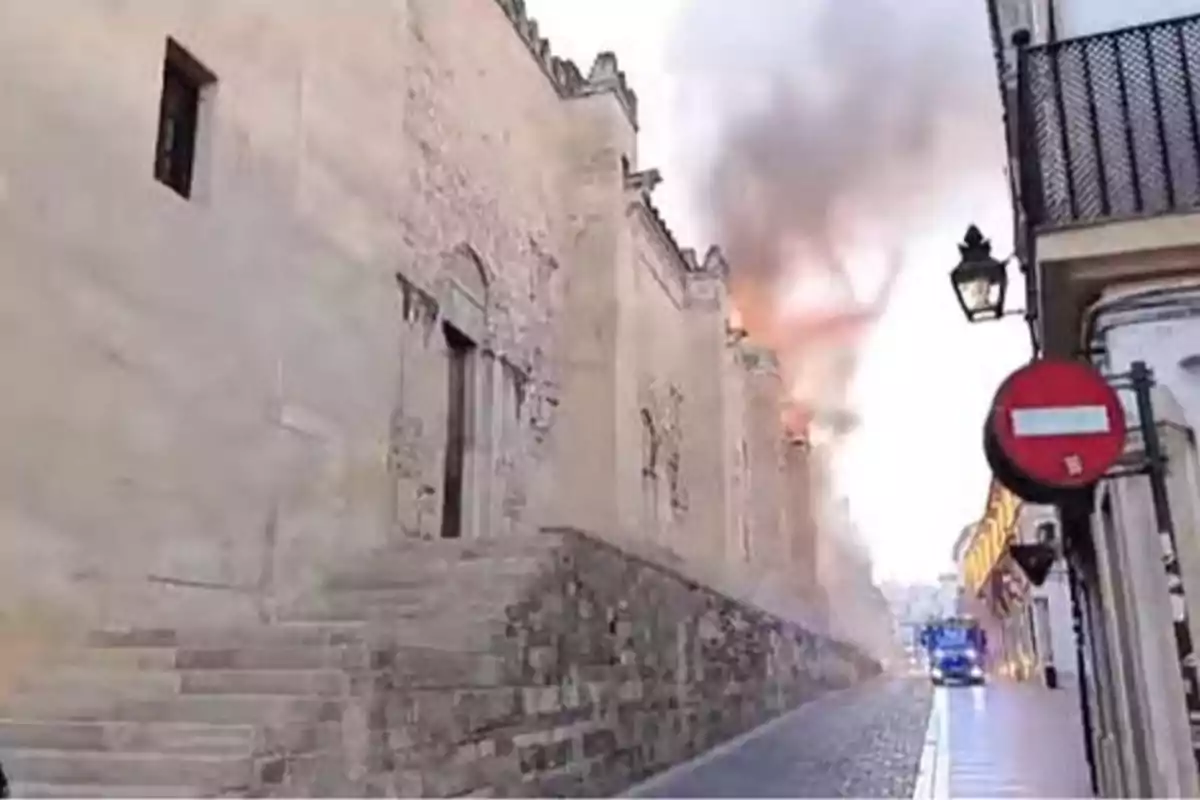 Fachada de un edificio antiguo con humo saliendo de su interior mientras un camión de bomberos se aproxima por una calle estrecha Fachada de un edificio antiguo con humo saliendo de su interior mientras un camión de bomberos se aproxima por una calle estrecha