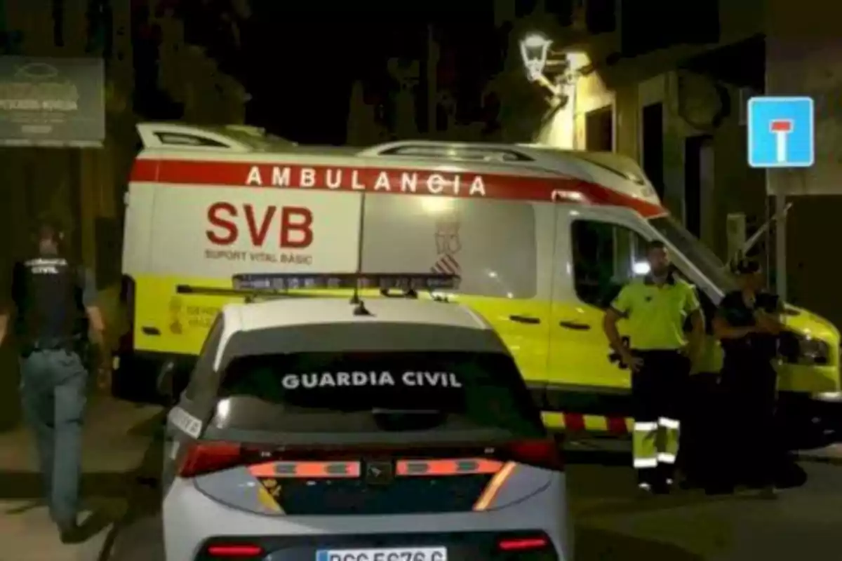 Una ambulancia y un coche de la Guardia Civil están estacionados en una calle de noche con varios agentes presentes