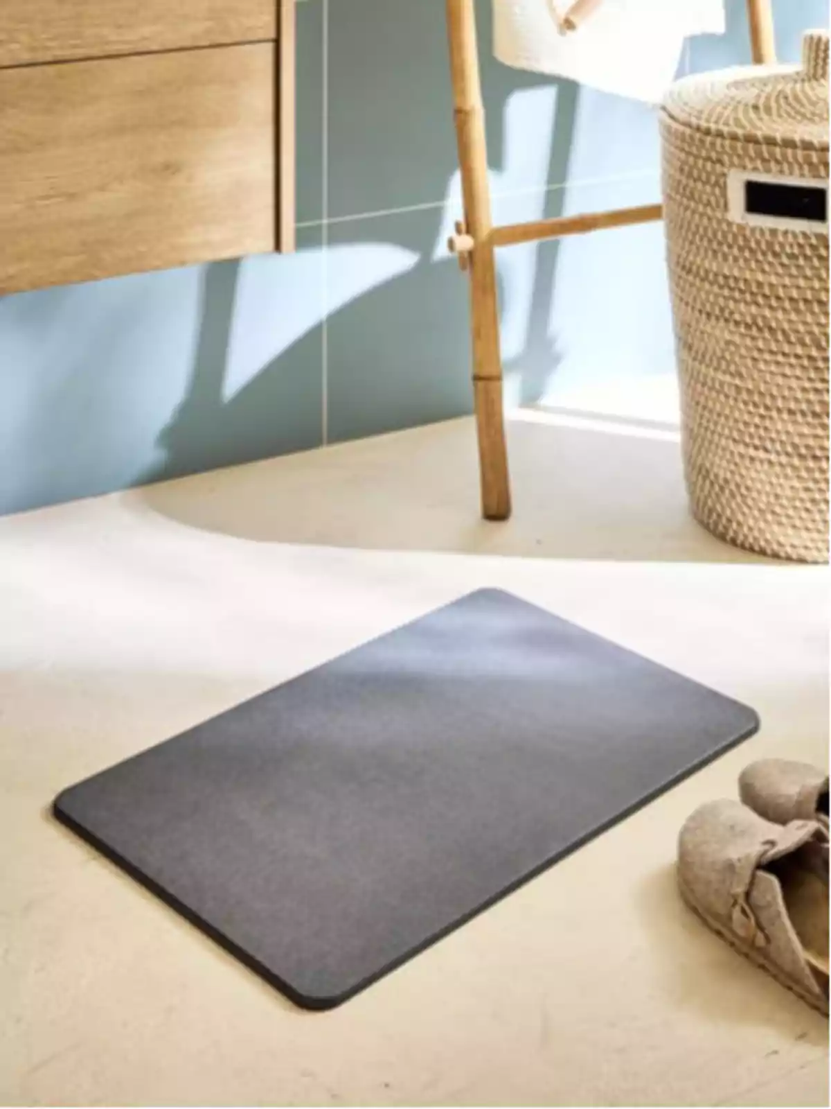 Tapete rectangular gris en el suelo de un baño junto a un cesto tejido y unas pantuflas beige Tapete rectangular gris en el suelo de un baño junto a un cesto tejido y unas pantuflas beige