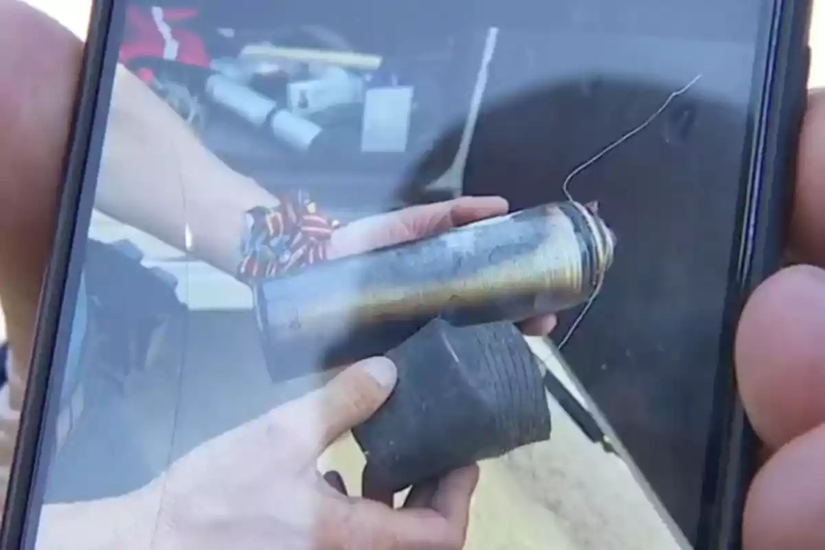 Persona sosteniendo un objeto cilíndrico metálico y una pieza negra frente a la cámara de un teléfono móvil Persona sosteniendo un objeto cilíndrico metálico y una pieza negra frente a la cámara de un teléfono móvil