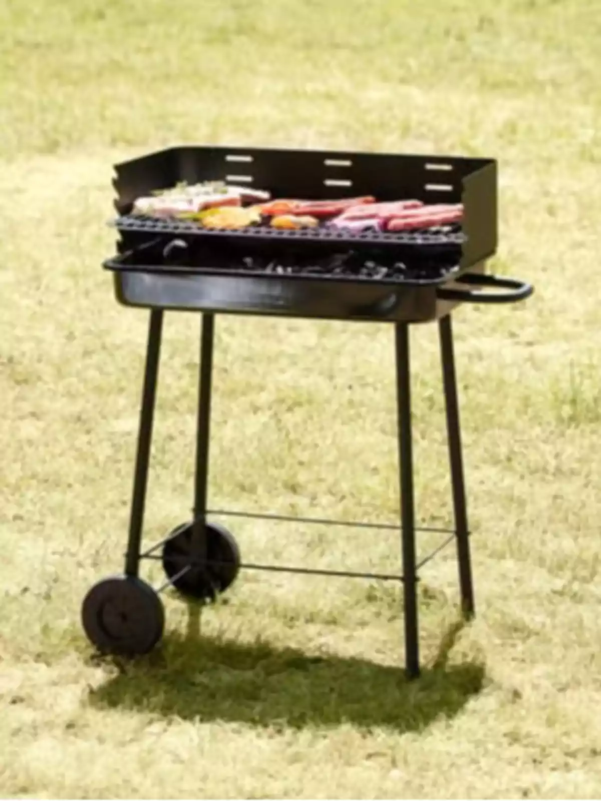 Parrilla de carbón portátil con ruedas en un jardín asando carne y verduras Parrilla de carbón portátil con ruedas en un jardín asando carne y verduras
