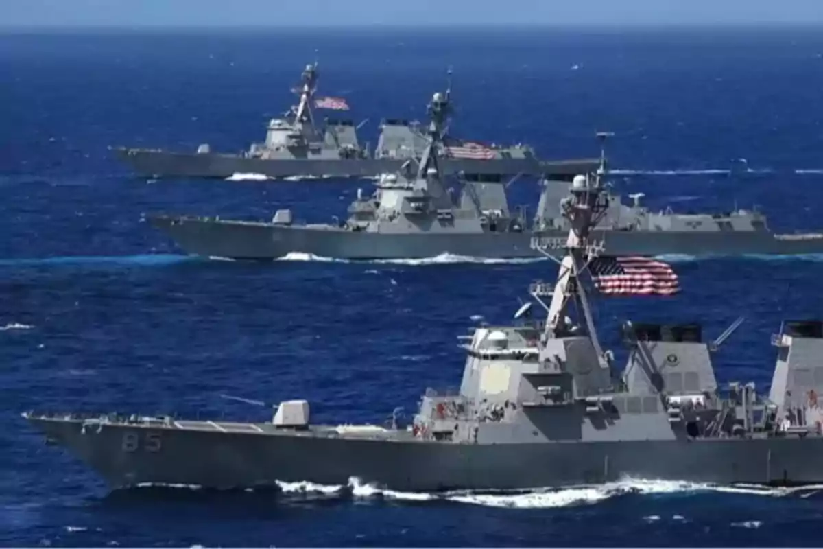 Tres buques de guerra navegando en formación sobre el mar con banderas de Estados Unidos ondeando Tres buques de guerra navegando en formación sobre el mar con banderas de Estados Unidos ondeando