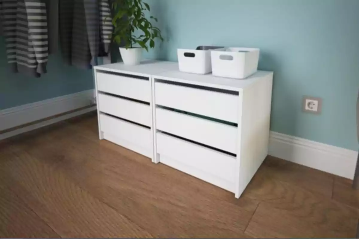 Dos cajoneras blancas con tres cajones cada una, sobre un suelo de madera, con una planta en maceta y dos cajas blancas encima, junto a una pared azul claro Dos cajoneras blancas con tres cajones cada una, sobre un suelo de madera, con una planta en maceta y dos cajas blancas encima, junto a una pared azul claro
