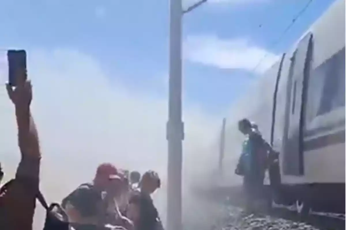 Personas evacuando un tren detenido en medio de una nube de humo bajo un cielo despejado Personas evacuando un tren detenido en medio de una nube de humo bajo un cielo despejado