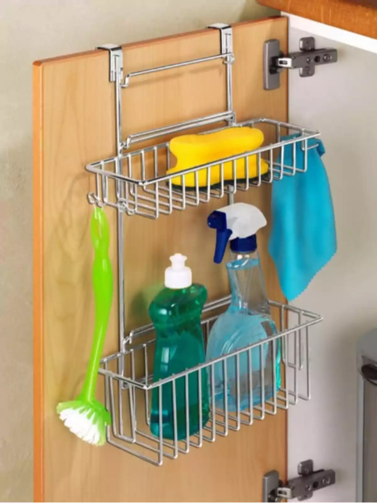 Organizador metálico colgado en la puerta de un gabinete de cocina con esponja amarilla, trapo azul, cepillo verde, botella de detergente y rociador de limpieza Organizador metálico colgado en la puerta de un gabinete de cocina con esponja amarilla, trapo azul, cepillo verde, botella de detergente y rociador de limpieza