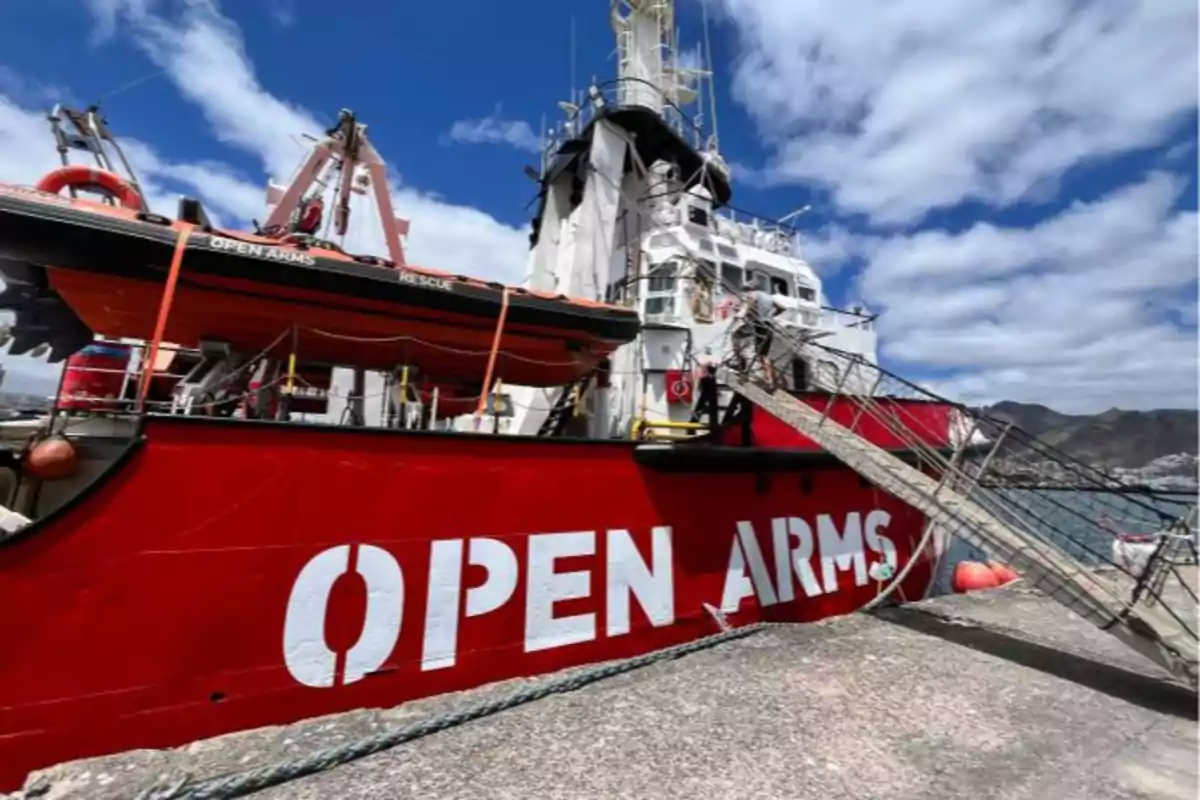 Barco de rescate Open Arms atracado en un puerto bajo un cielo parcialmente nublado Barco de rescate Open Arms atracado en un puerto bajo un cielo parcialmente nublado