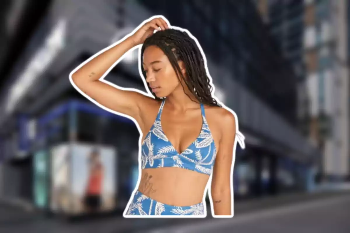 Mujer con trenzas usando un conjunto azul con estampado de hojas posando con el brazo levantado sobre la cabeza frente a un fondo urbano desenfocado Mujer con trenzas usando un conjunto azul con estampado de hojas posando con el brazo levantado sobre la cabeza frente a un fondo urbano desenfocado