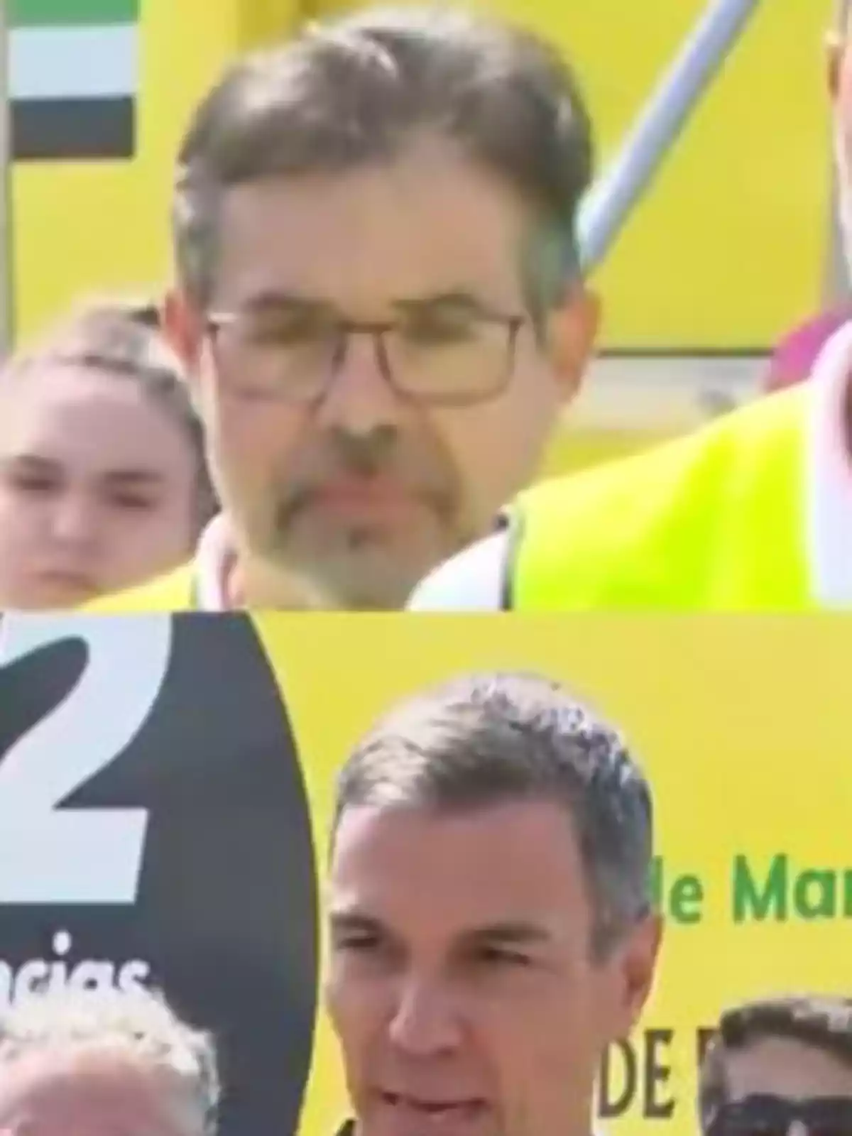 Dos hombres en un evento al aire libre con fondo amarillo y personas alrededor Dos hombres en un evento al aire libre con fondo amarillo y personas alrededor