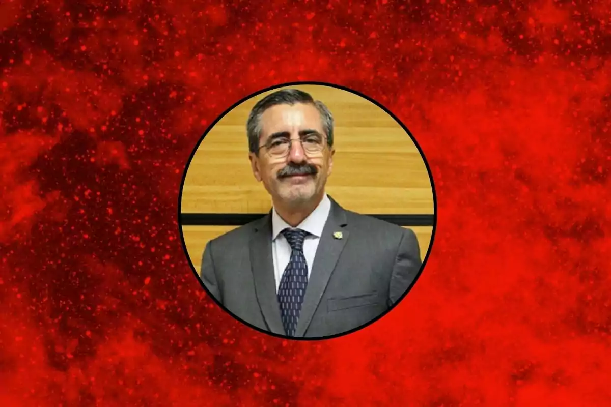 Hombre de cabello canoso y bigote con gafas y traje formal dentro de un círculo sobre un fondo rojo texturizado