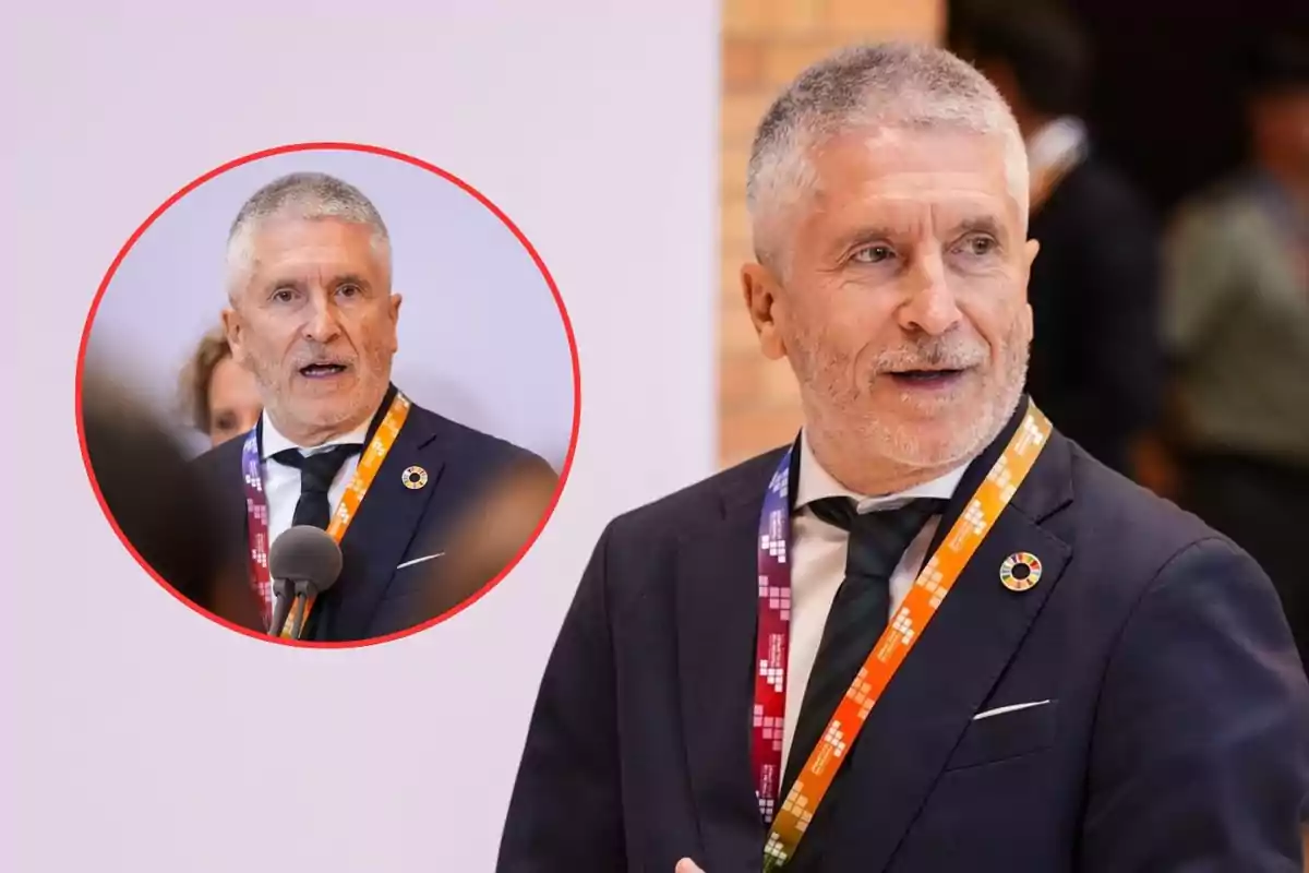 Hombre de cabello canoso y barba corta con traje oscuro y corbata, usando un gafete colorido y un pin redondo, hablando en un evento con fondo desenfocado y un círculo rojo que muestra un primer plano de él mismo hablando frente a un micrófono.