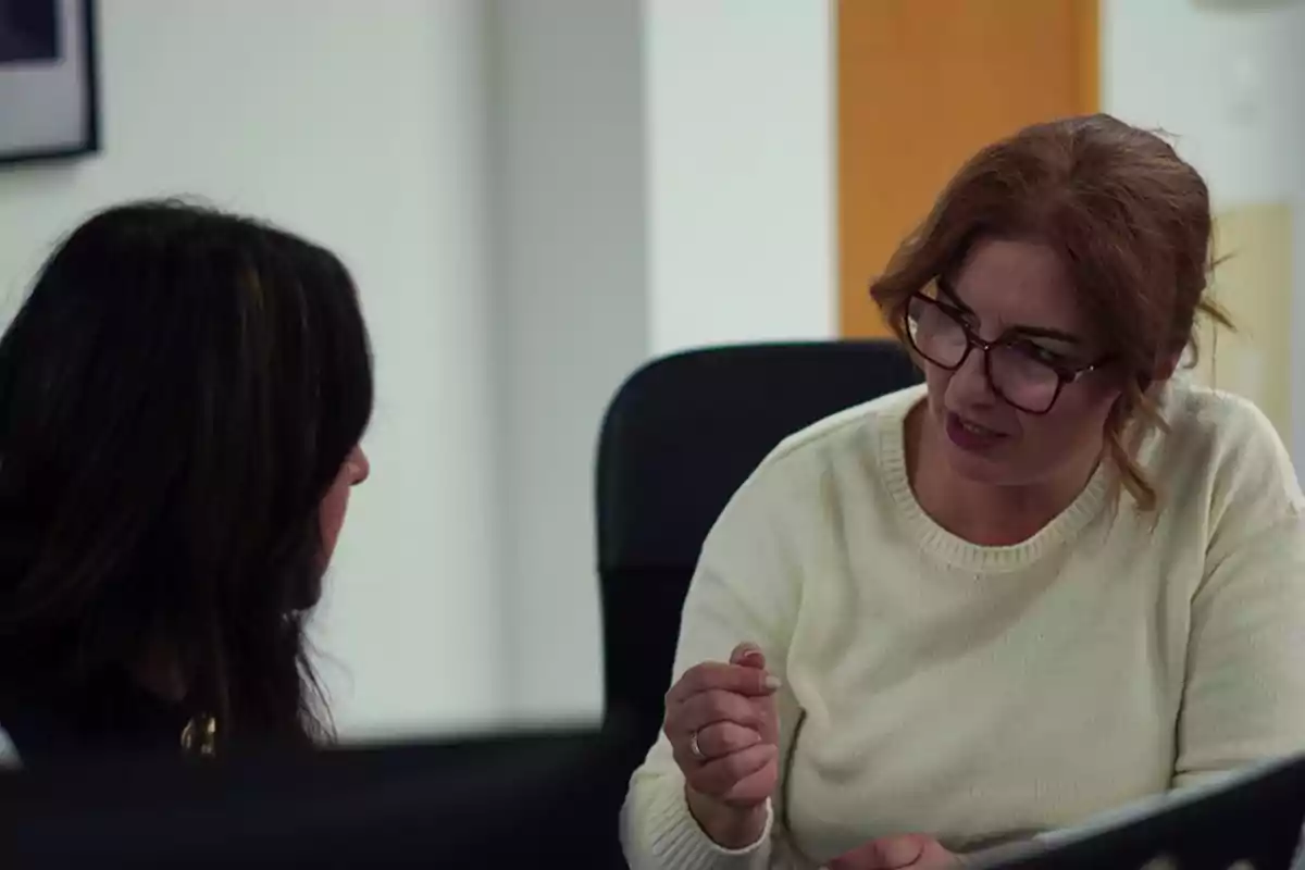 Dos mujeres conversan en una oficina mientras una de ellas gesticula con la mano