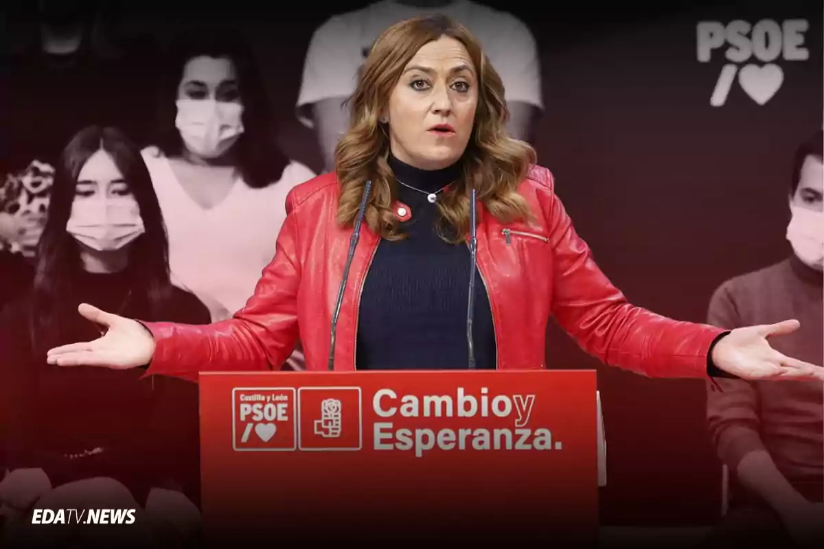 Mujer con chaqueta roja hablando en un atril del PSOE con el lema Cambio y Esperanza y personas con mascarilla al fondo