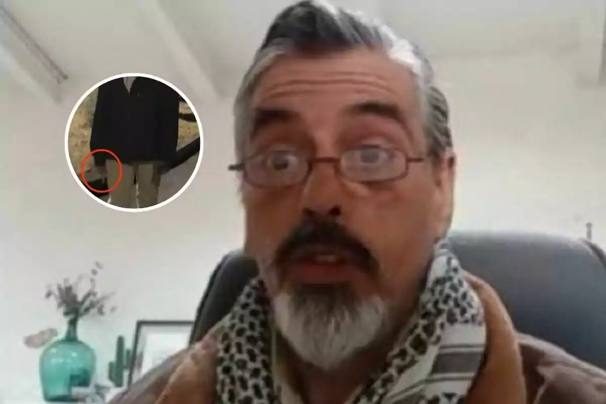 Hombre de cabello canoso y barba con expresión de sorpresa usando gafas y bufanda, sentado en una oficina con una planta y un cuadro al fondo, con un recuadro en la esquina que muestra a una persona de pie y un círculo rojo señalando un objeto en su mano.