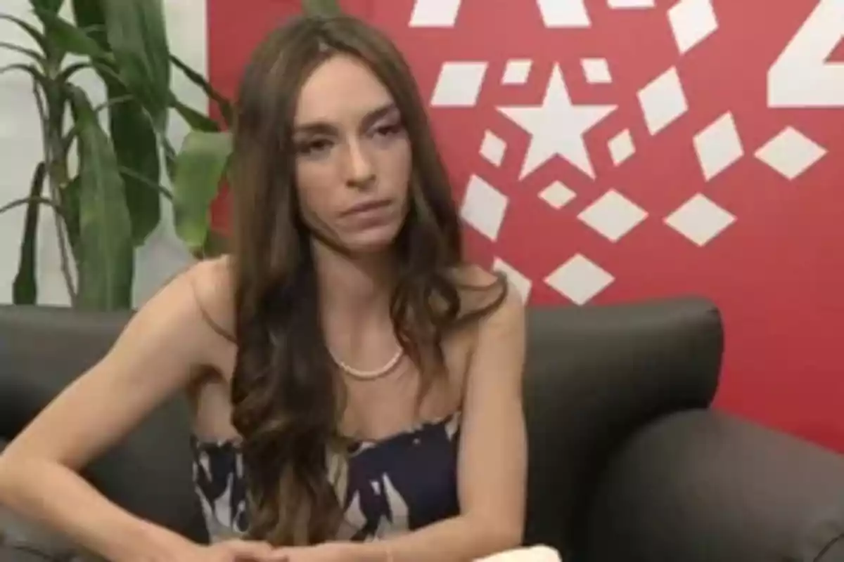 Mujer de cabello largo y suelto sentada en un sillón negro con fondo rojo decorado con figuras geométricas blancas y una planta al lado Mujer de cabello largo y suelto sentada en un sillón negro con fondo rojo decorado con figuras geométricas blancas y una planta al lado