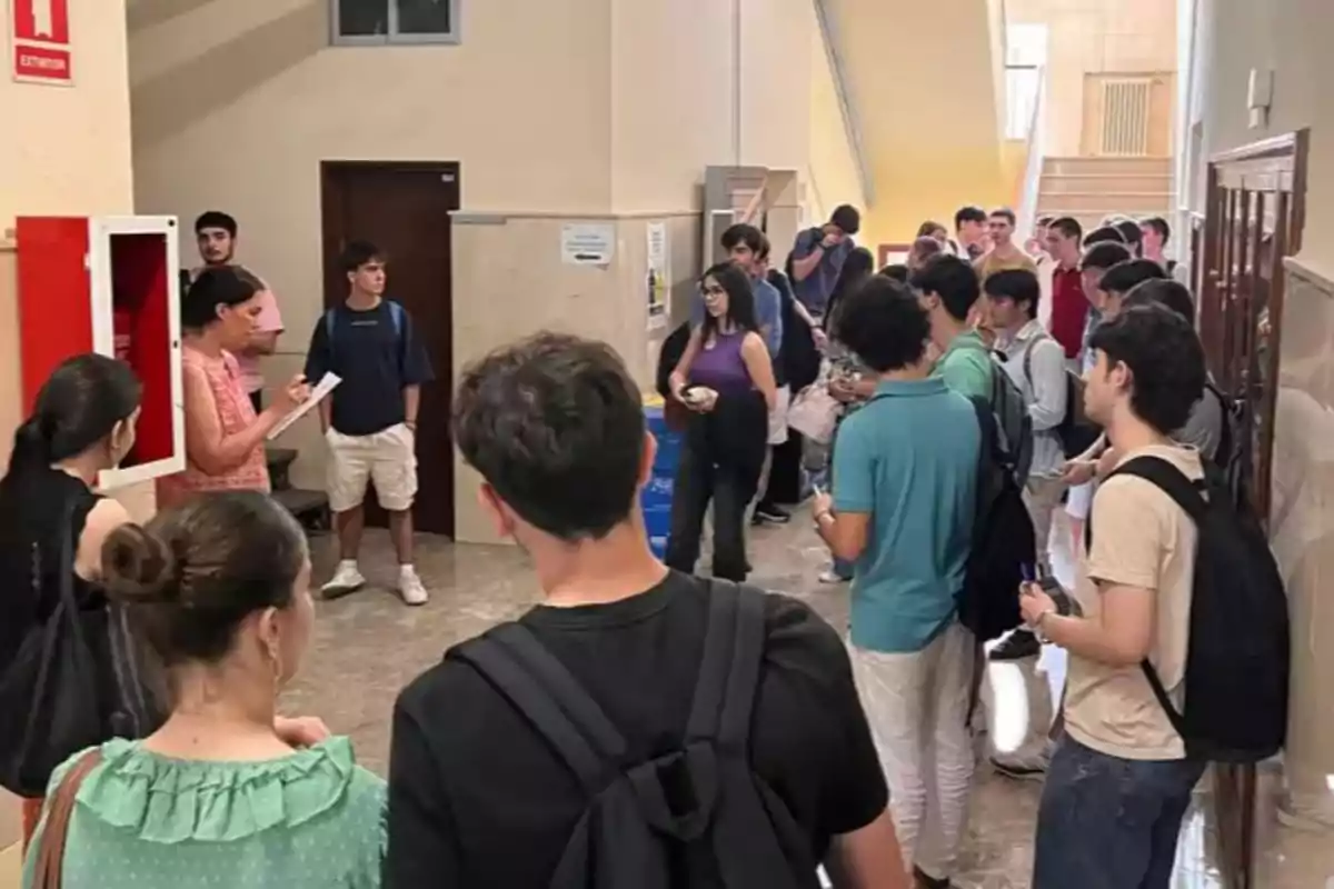 Un grupo de estudiantes espera en un pasillo de una escuela mientras una mujer toma lista con una libreta en la mano Un grupo de estudiantes espera en un pasillo de una escuela mientras una mujer toma lista con una libreta en la mano