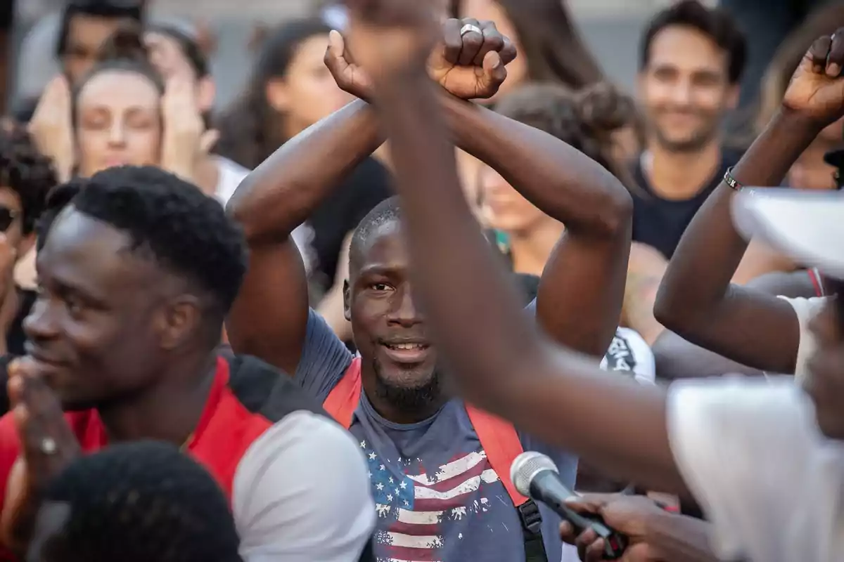 Hombre en una manifestación levantando los brazos cruzados sobre la cabeza rodeado de otras personas Hombre en una manifestación levantando los brazos cruzados sobre la cabeza rodeado de otras personas