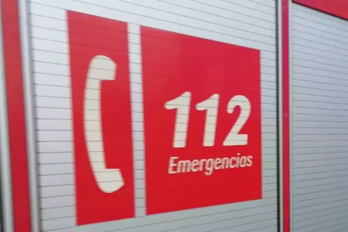 Panel rojo con el número 112 y la palabra emergencias junto a un icono de teléfono sobre una superficie metálica Panel rojo con el número 112 y la palabra emergencias junto a un icono de teléfono sobre una superficie metálica