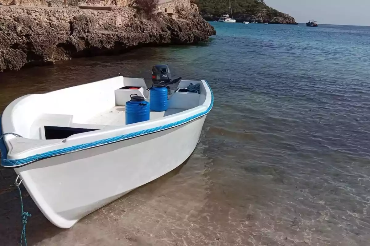 Barca blanca pequeña amarrada en la orilla de una playa con agua cristalina y rocas al fondo Barca blanca pequeña amarrada en la orilla de una playa con agua cristalina y rocas al fondo