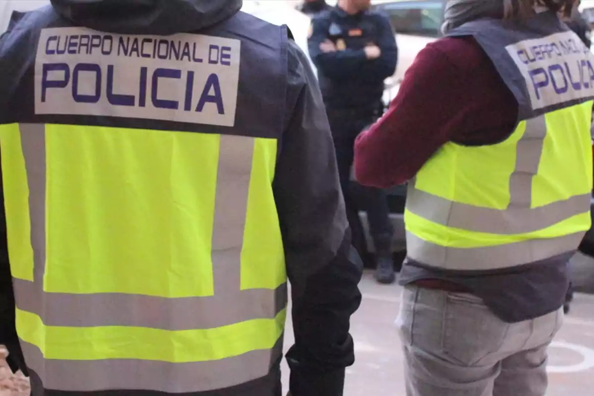 Dos agentes de policía con chalecos reflectantes amarillos y la leyenda Cuerpo Nacional de Policía en la espalda están de pie en la calle Dos agentes de policía con chalecos reflectantes amarillos y la leyenda Cuerpo Nacional de Policía en la espalda están de pie en la calle