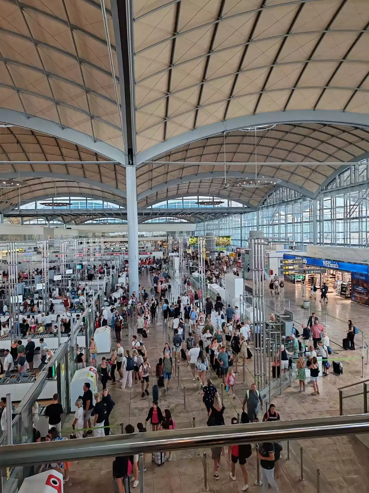 Terminal de aeropuerto con muchas personas haciendo fila y caminando bajo un techo amplio y curvado Terminal de aeropuerto con muchas personas haciendo fila y caminando bajo un techo amplio y curvado