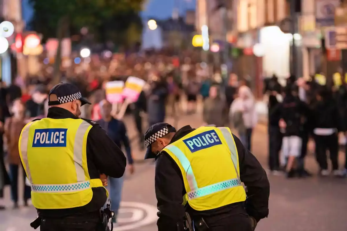 Dos policías con chalecos amarillos observan una multitud en una calle durante una manifestación o protesta