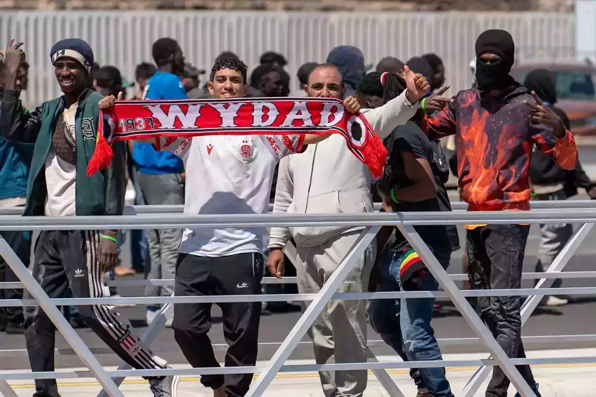 Un grupo de jóvenes sonríe y posa detrás de una valla mientras uno de ellos sostiene una bufanda roja del equipo Wydad Un grupo de jóvenes sonríe y posa detrás de una valla mientras uno de ellos sostiene una bufanda roja del equipo Wydad
