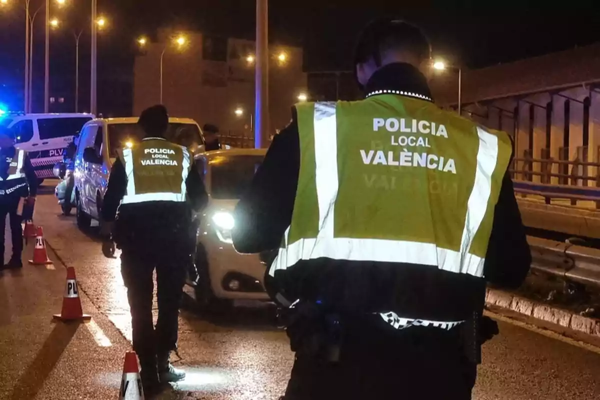 Agentes de la Policía Local de Valencia realizan un control de tráfico nocturno en una carretera iluminada con conos y vehículos detenidos.