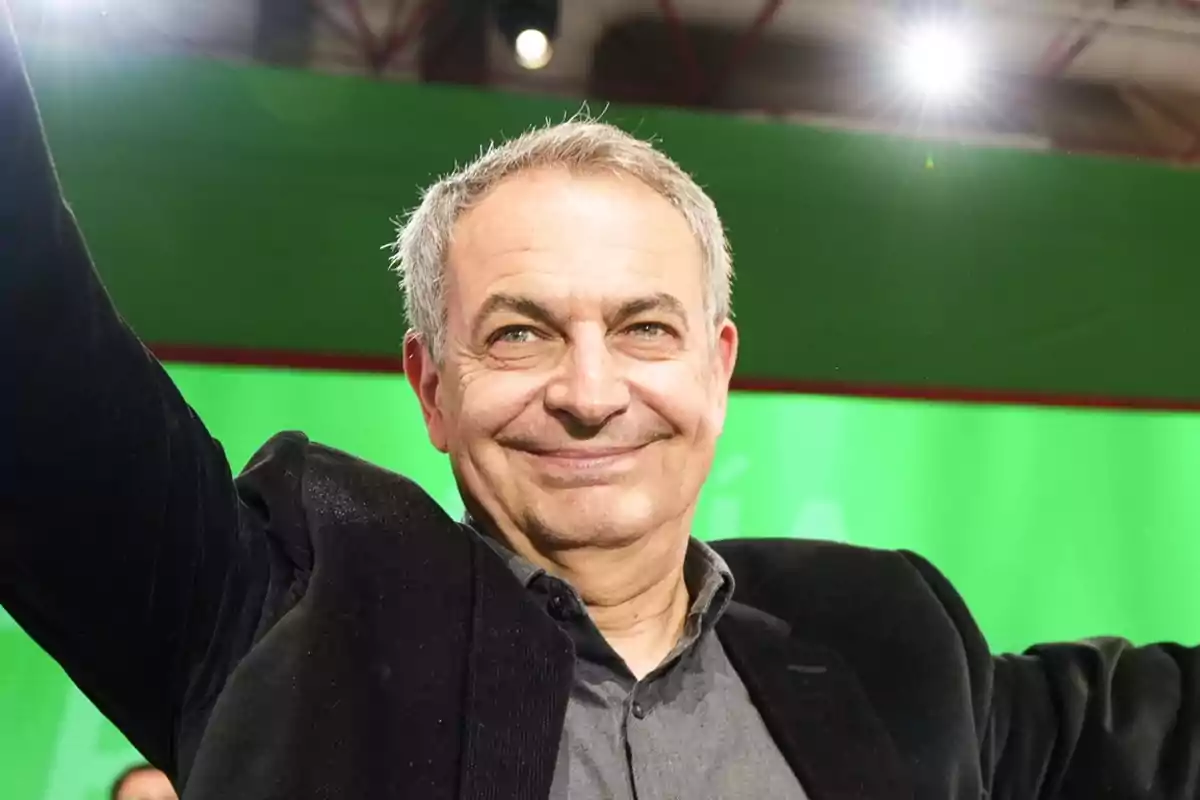 Hombre de cabello canoso sonriente con los brazos levantados frente a un fondo verde