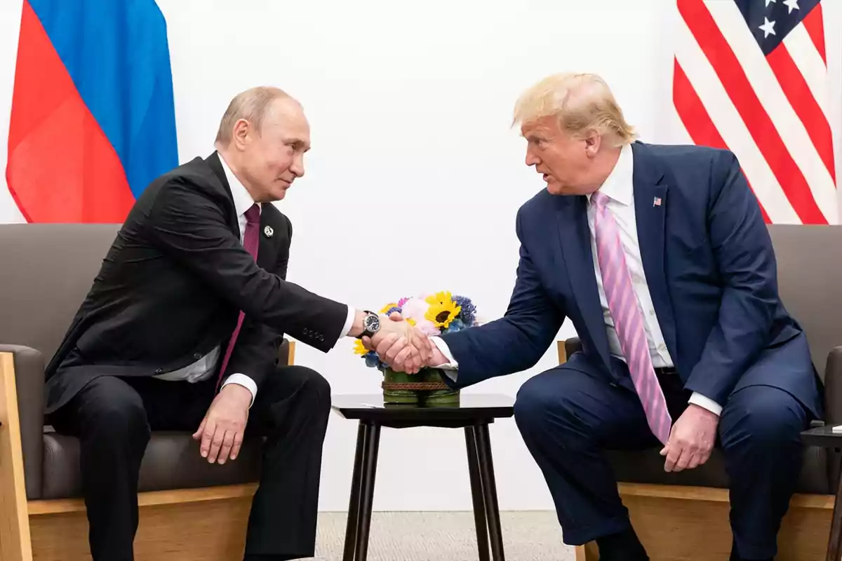 Dos hombres de traje se dan la mano sentados frente a frente con banderas de Rusia y Estados Unidos al fondo Dos hombres de traje se dan la mano sentados frente a frente con banderas de Rusia y Estados Unidos al fondo