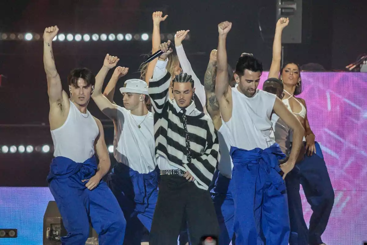 Grupo de bailarines y un cantante en el centro realizan una coreografía en el escenario durante un concierto con luces de fondo Grupo de bailarines y un cantante en el centro realizan una coreografía en el escenario durante un concierto con luces de fondo