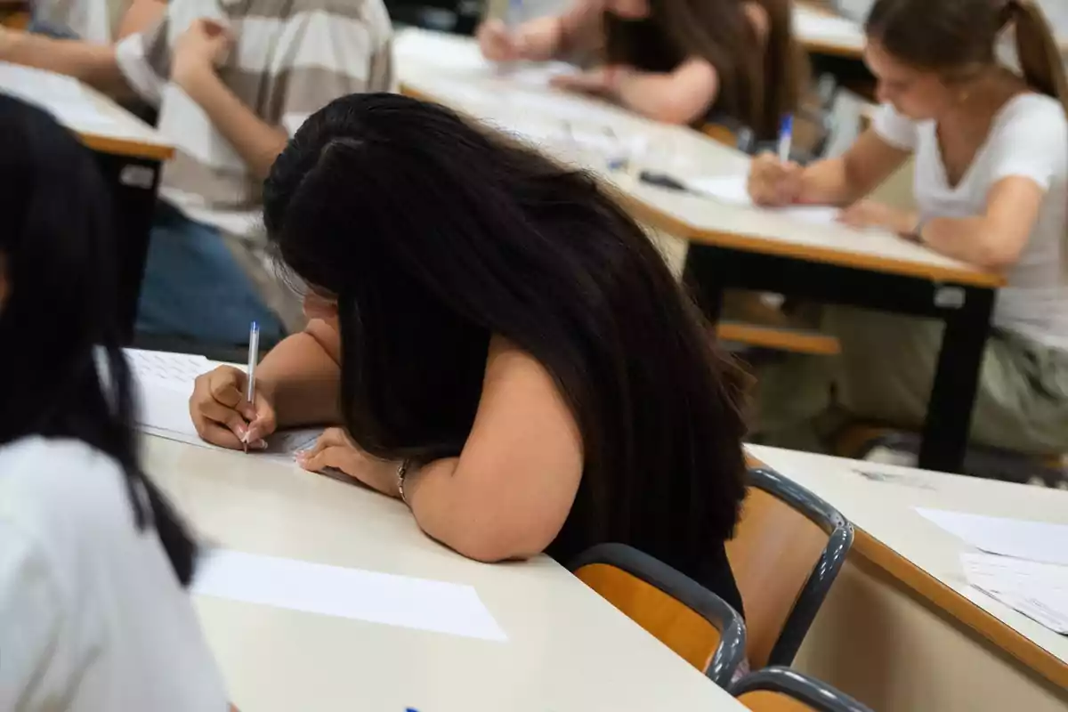 Estudiantes sentados en pupitres escribiendo durante un examen en un aula Estudiantes sentados en pupitres escribiendo durante un examen en un aula