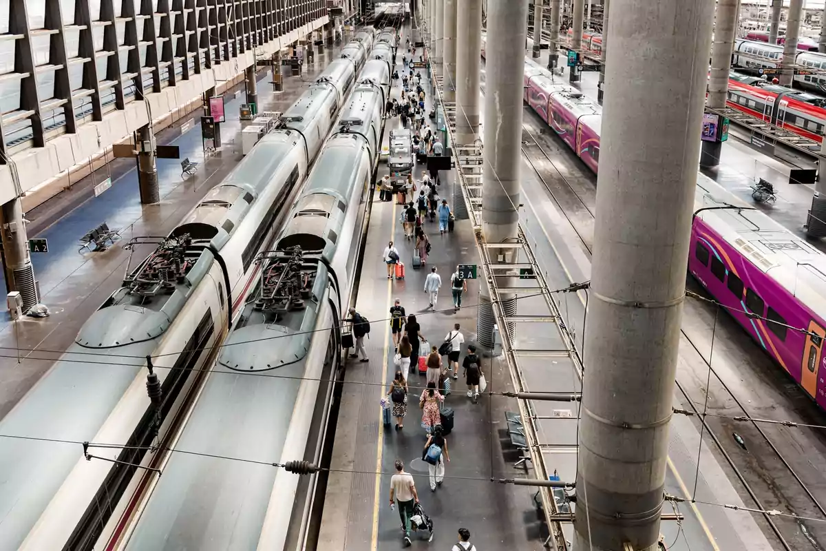 Vista aérea de una estación de tren con varias personas caminando por el andén y trenes de diferentes colores estacionados Vista aérea de una estación de tren con varias personas caminando por el andén y trenes de diferentes colores estacionados