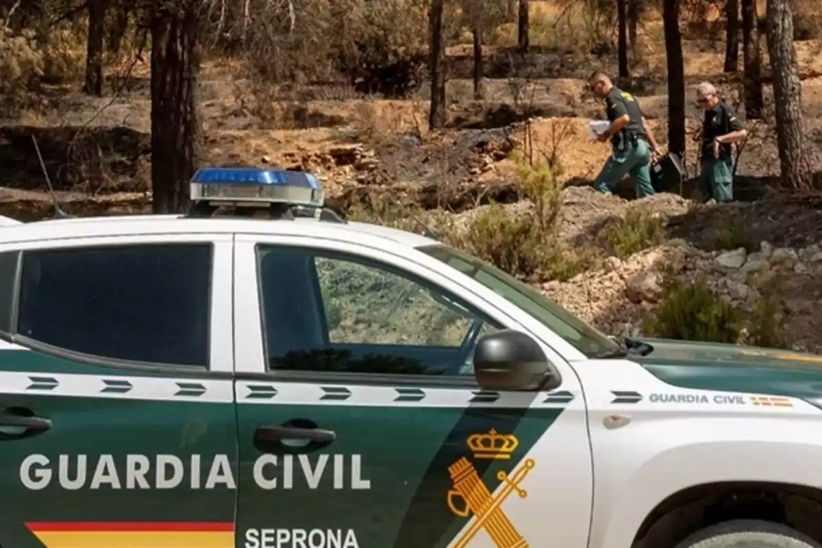 Vehículo de la Guardia Civil estacionado en un área forestal mientras dos agentes caminan entre los árboles y la vegetación