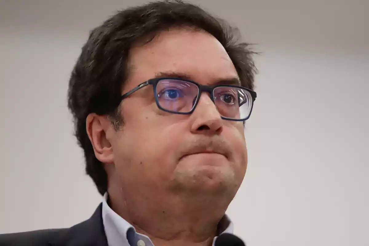 Hombre de cabello oscuro y gafas con expresión seria mirando hacia el frente
