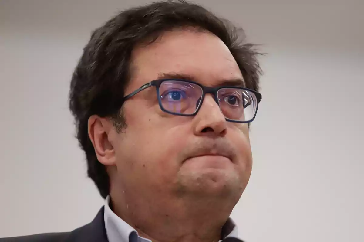 Hombre de cabello oscuro y gafas mirando hacia el frente con expresión seria Hombre de cabello oscuro y gafas mirando hacia el frente con expresión seria