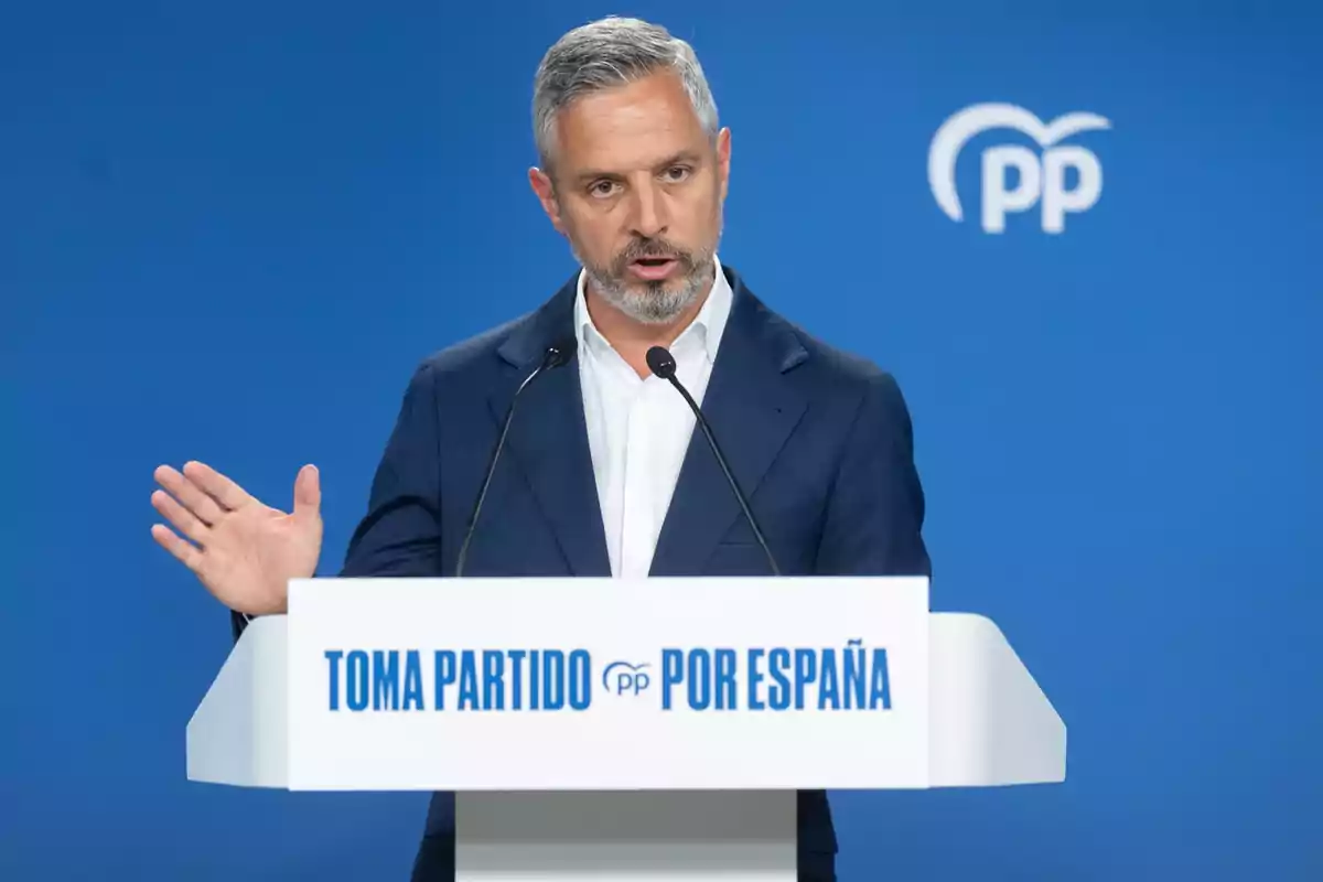 Hombre de cabello canoso y barba hablando en un atril con el texto Toma Partido por España sobre un fondo azul con el logo del Partido Popular