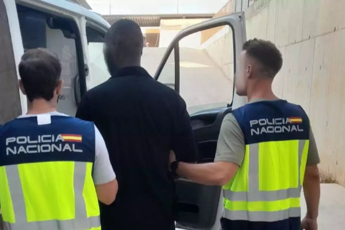 Dos agentes de la Policía Nacional escoltan a una persona hacia una furgoneta policial