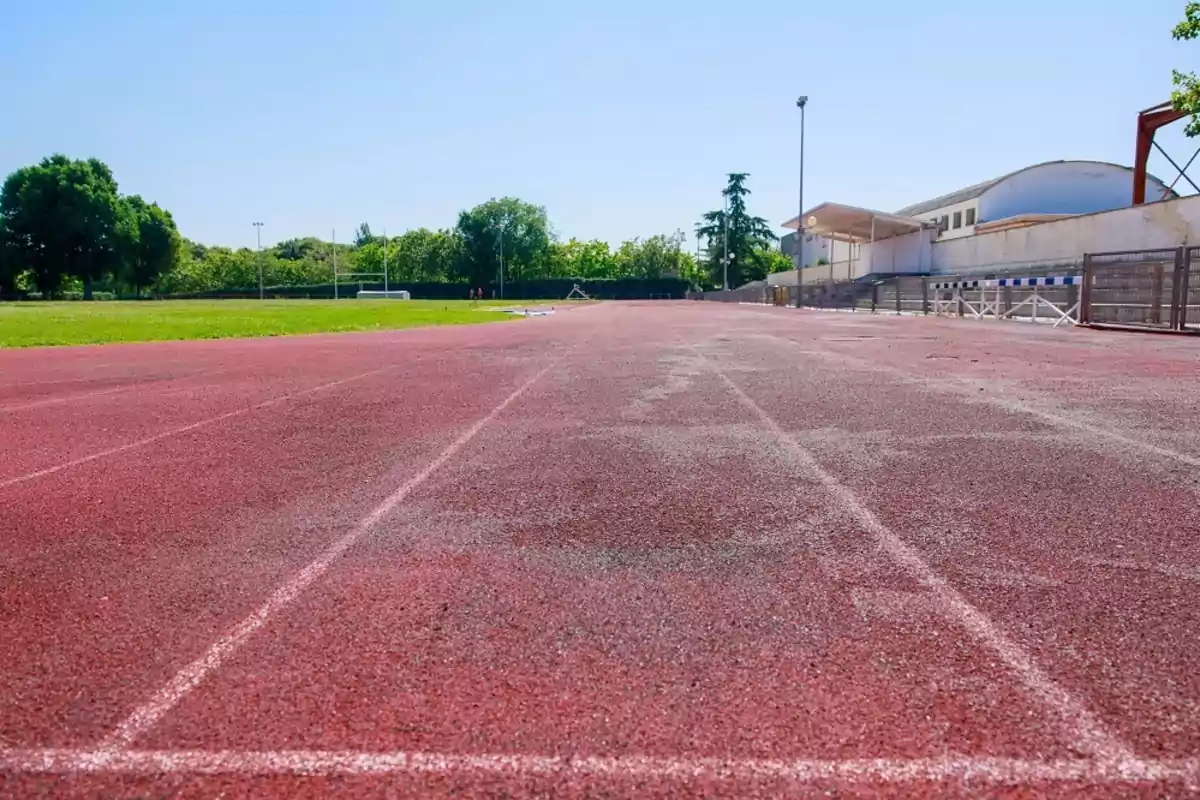 Pista de atletismo al aire libre con césped y gradas a un lado en un día soleado