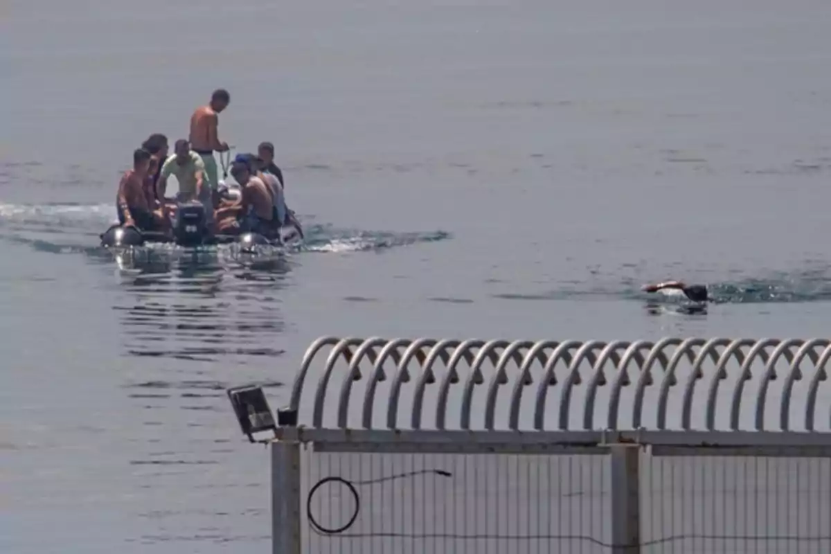 Un grupo de personas viaja en una lancha inflable mientras una persona nada cerca de una valla metálica en el mar. Un grupo de personas viaja en una lancha inflable mientras una persona nada cerca de una valla metálica en el mar.