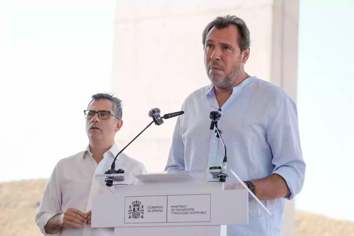 Dos hombres de pie junto a un atril con micrófonos en un evento al aire libre del Ministerio de Transportes y Movilidad Sostenible del Gobierno de España Dos hombres de pie junto a un atril con micrófonos en un evento al aire libre del Ministerio de Transportes y Movilidad Sostenible del Gobierno de España