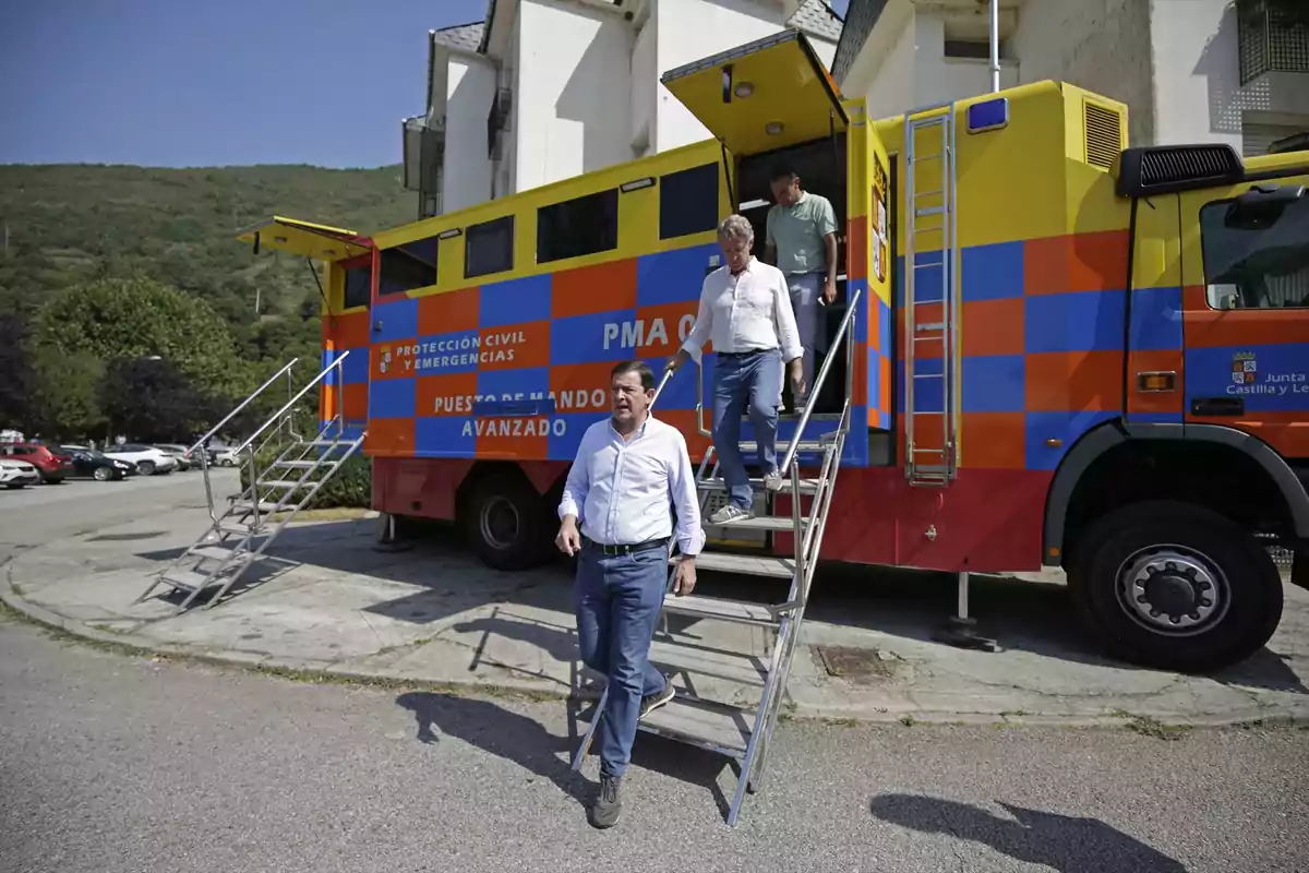 Tres personas bajan por las escaleras de un camión de emergencias de Protección Civil estacionado en una zona urbana con montañas al fondo. Tres personas bajan por las escaleras de un camión de emergencias de Protección Civil estacionado en una zona urbana con montañas al fondo.