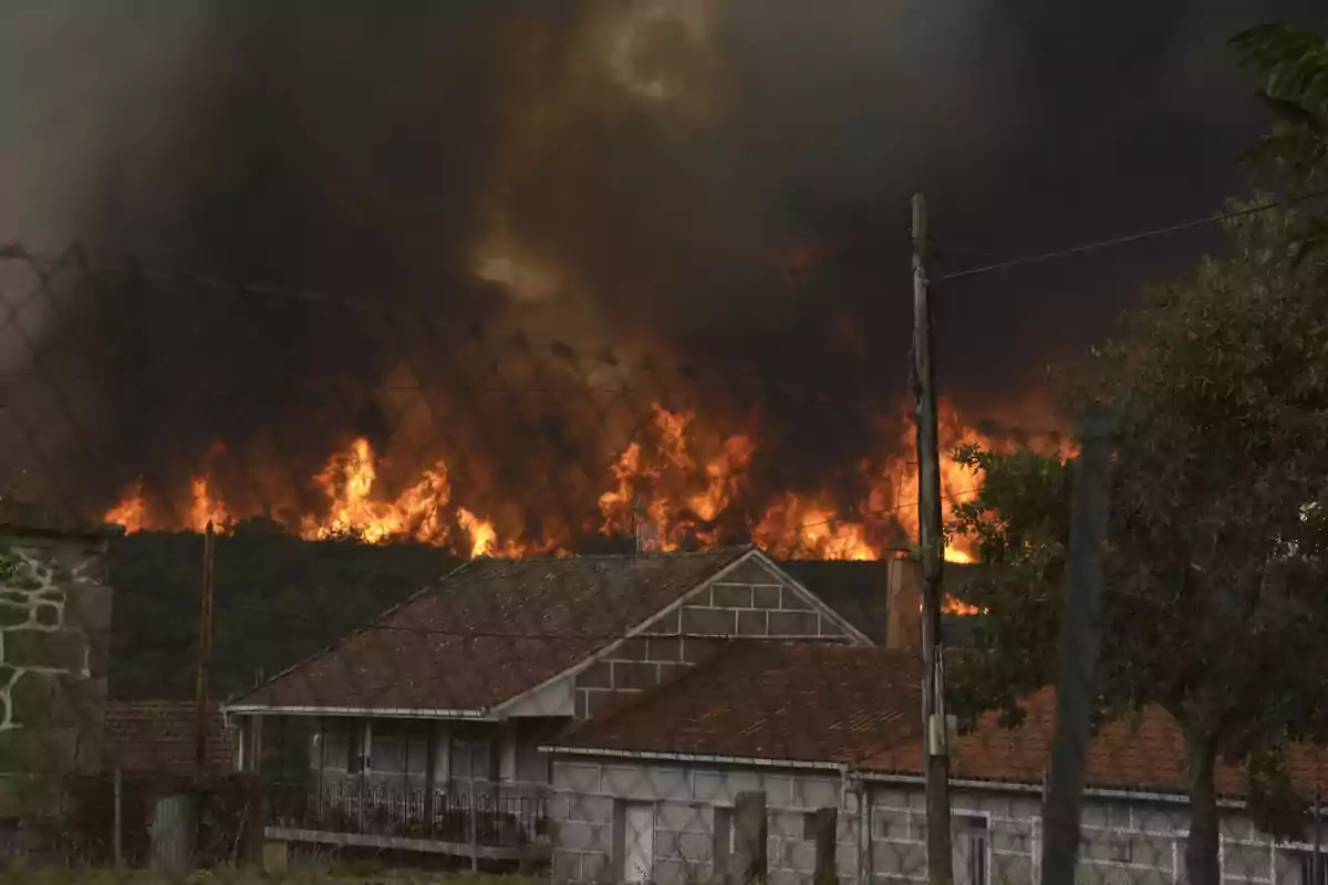 Incendio forestal acercándose peligrosamente a una casa en una zona rural con humo denso cubriendo el cielo Incendio forestal acercándose peligrosamente a una casa en una zona rural con humo denso cubriendo el cielo