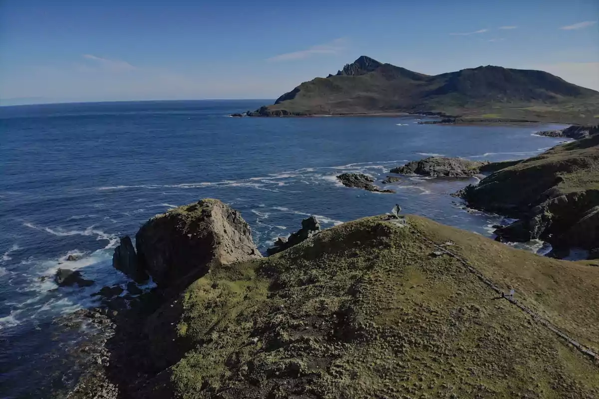 Vista panorámica de una costa rocosa con colinas verdes y el mar azul bajo un cielo despejado Vista panorámica de una costa rocosa con colinas verdes y el mar azul bajo un cielo despejado