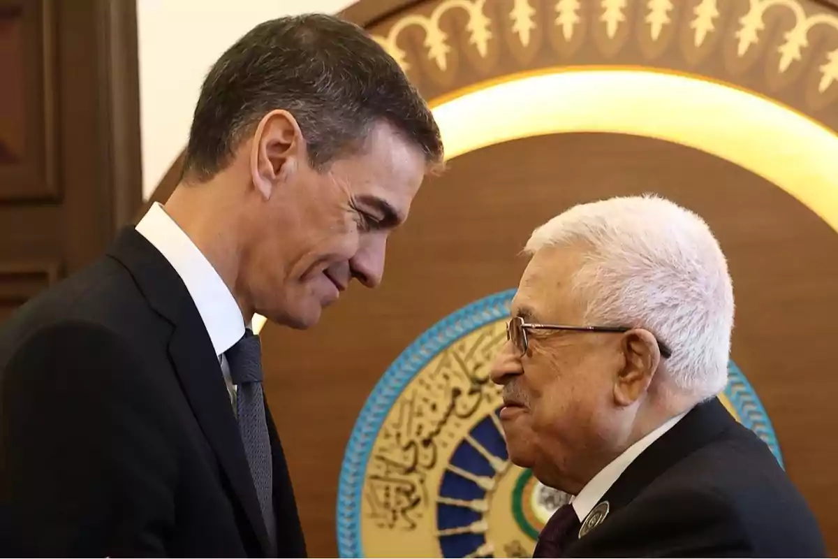 Dos hombres de traje se saludan cordialmente frente a un fondo decorativo con detalles dorados y azules Dos hombres de traje se saludan cordialmente frente a un fondo decorativo con detalles dorados y azules