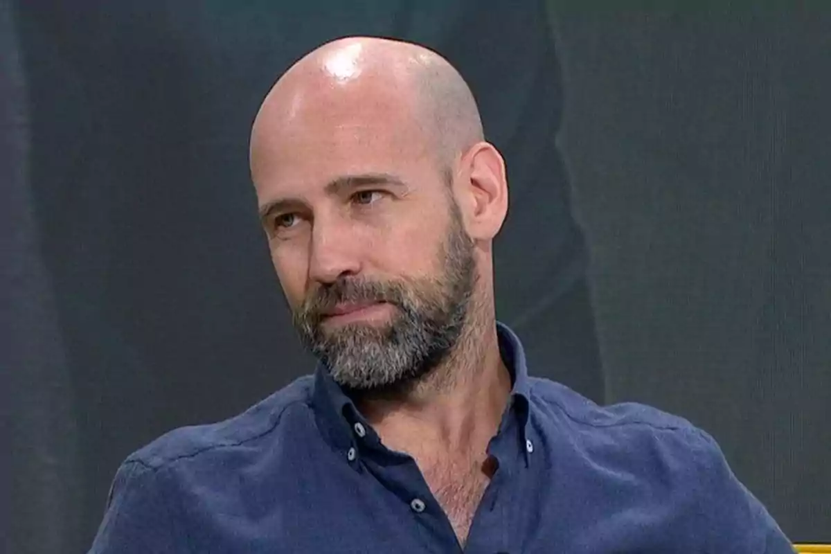 Hombre calvo con barba y camisa azul mirando hacia un lado en un entorno interior Hombre calvo con barba y camisa azul mirando hacia un lado en un entorno interior