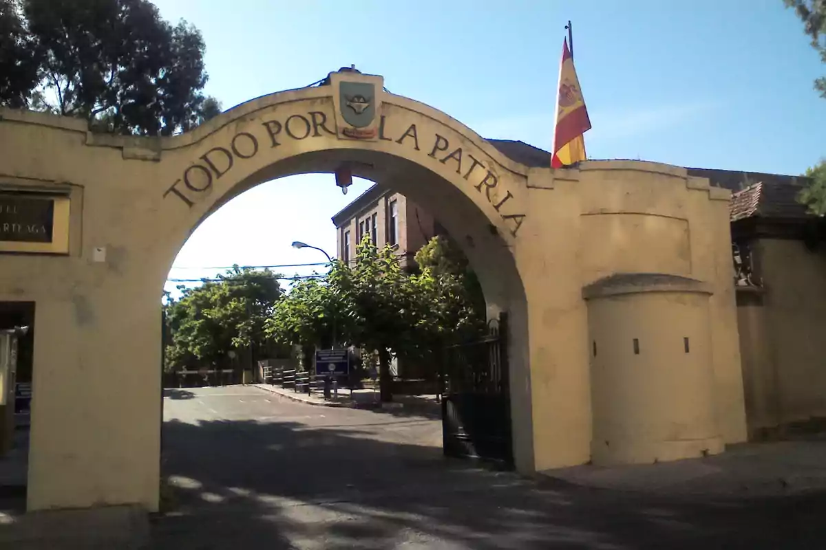 Entrada de un cuartel militar español con un arco amarillo que tiene la inscripción Todo por la patria y una bandera de España ondeando en la parte superior Entrada de un cuartel militar español con un arco amarillo que tiene la inscripción Todo por la patria y una bandera de España ondeando en la parte superior