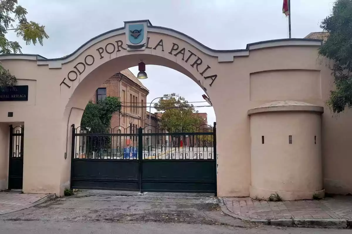Entrada principal de un cuartel militar con un arco que tiene la frase TODO POR LA PATRIA y un portón negro cerrado